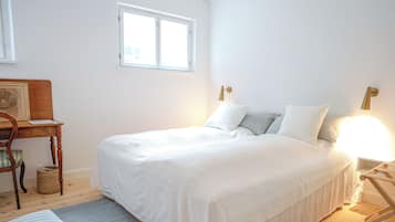 A bedroom with a large bed, a bedside table, a chair, and a window.
