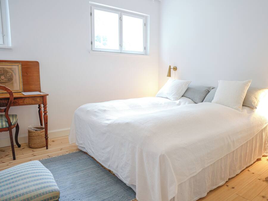 A bedroom with a large bed, a bedside table, a chair, and a window.