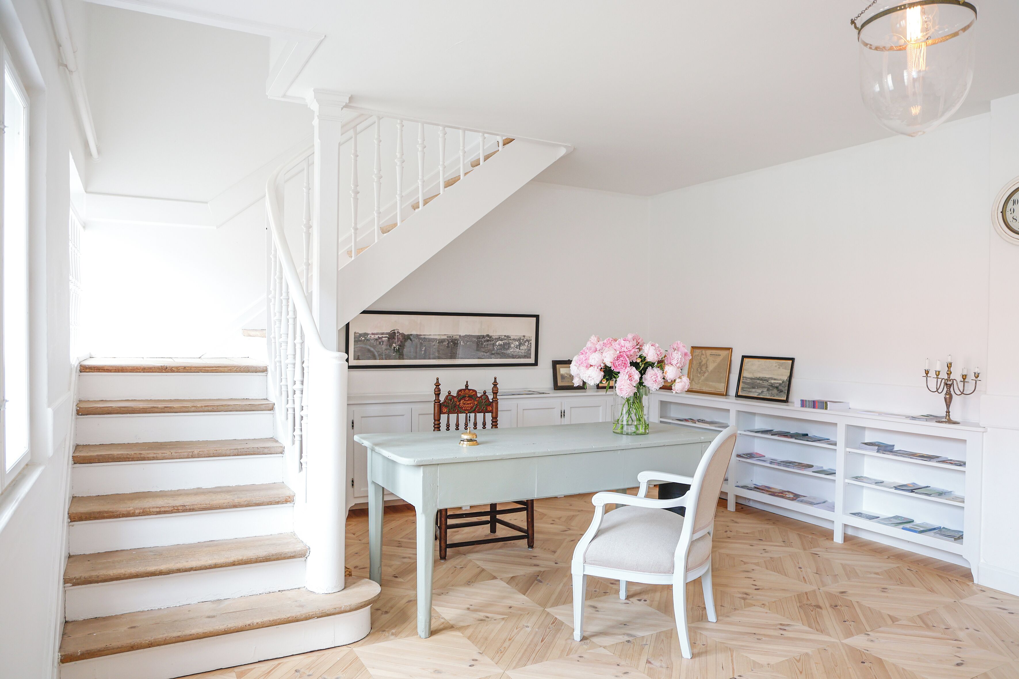 A staircase leading to a dining area with a table and chairs, a vase of flowers, and a bookshelf.
