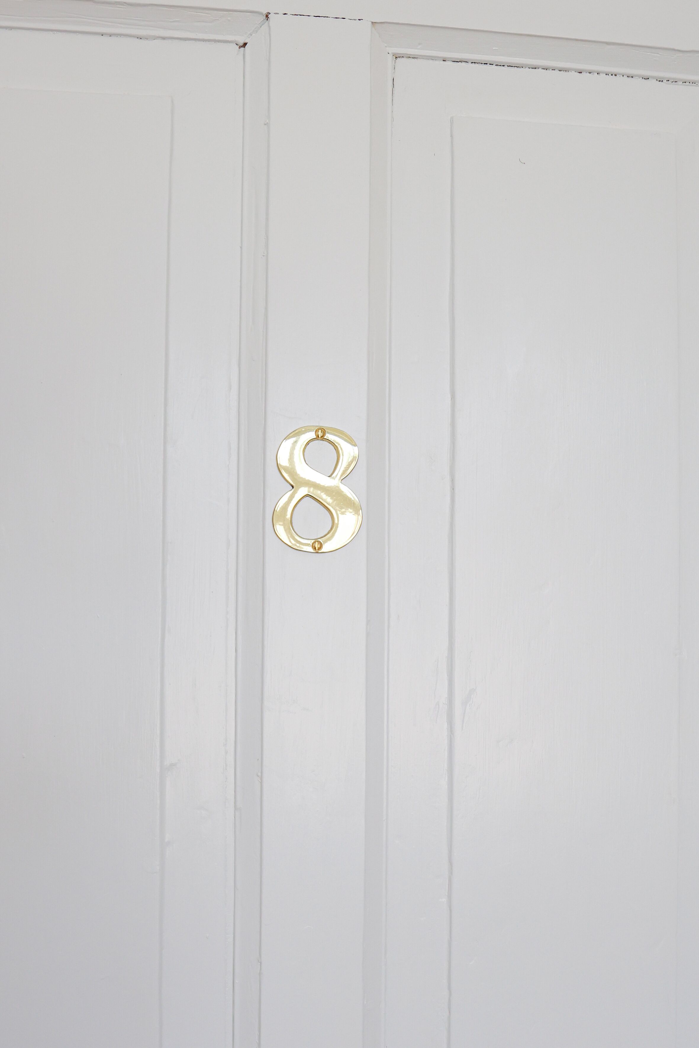 Une porte blanche avec une poignée en forme de chiffre 8, de couleur dorée.