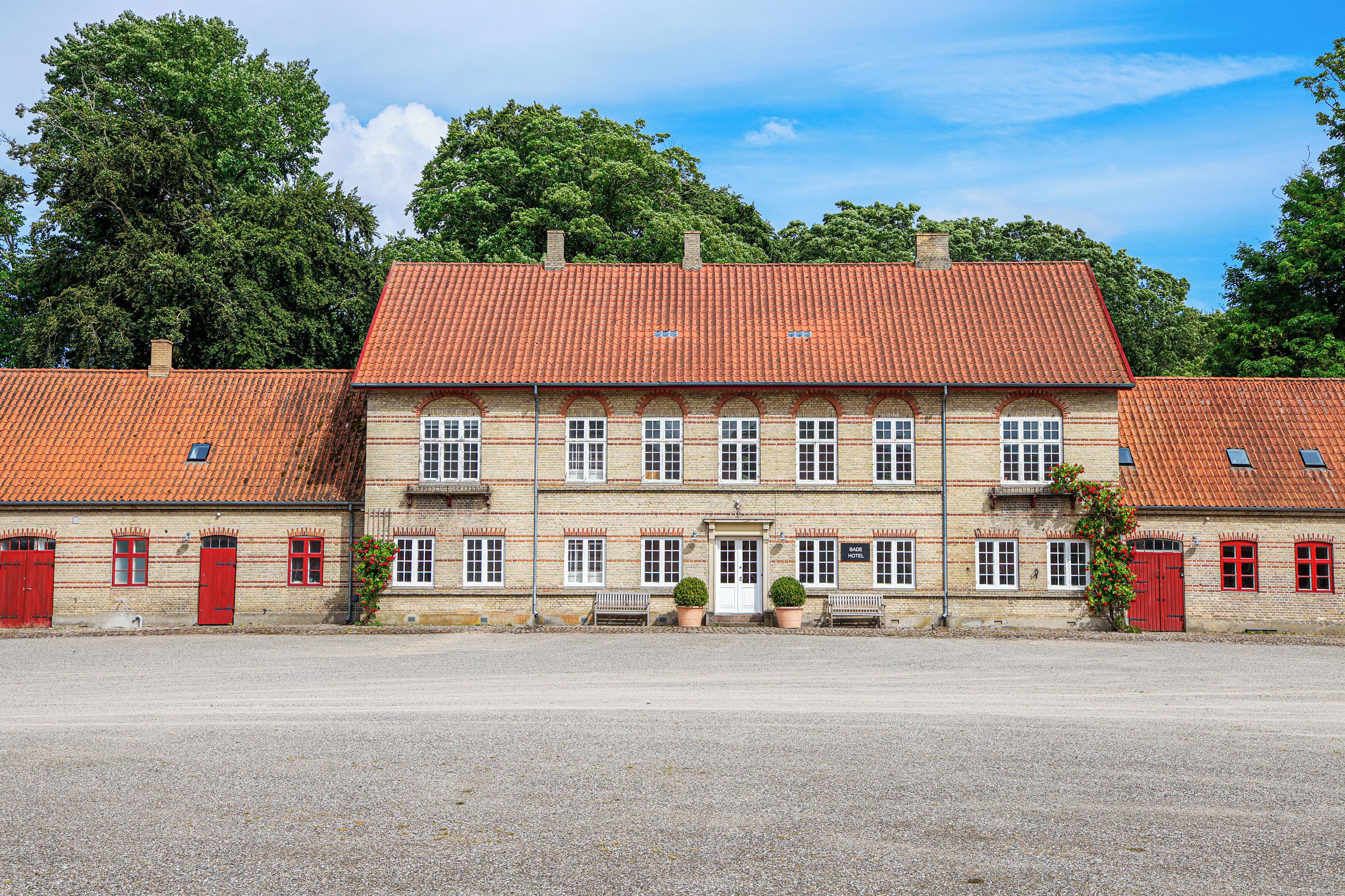 A two-story building with a red-tiled roof, multiple windows, and a sign indicating it is a hotel.