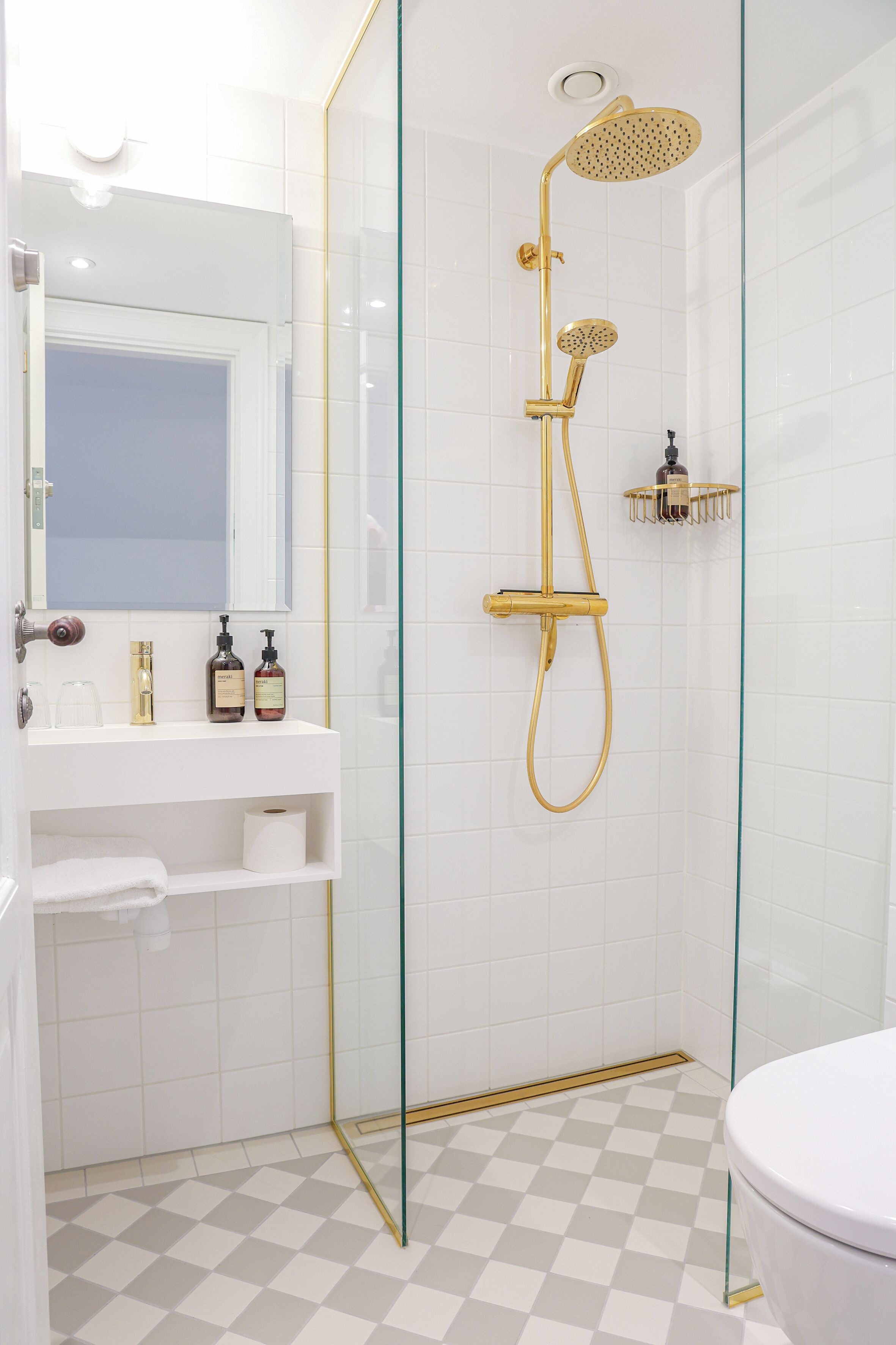Une salle de bain avec une douche à parois de verre, un lavabo blanc avec des robinets dorés et un carrelage à motifs géométriques.