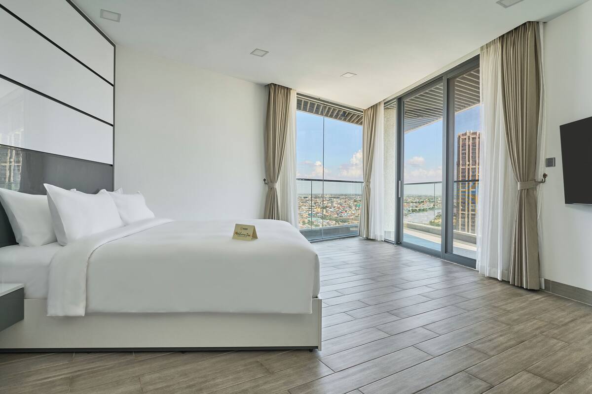 A modern hotel room with a large bed, a flat-screen TV, and a balcony with a city view.