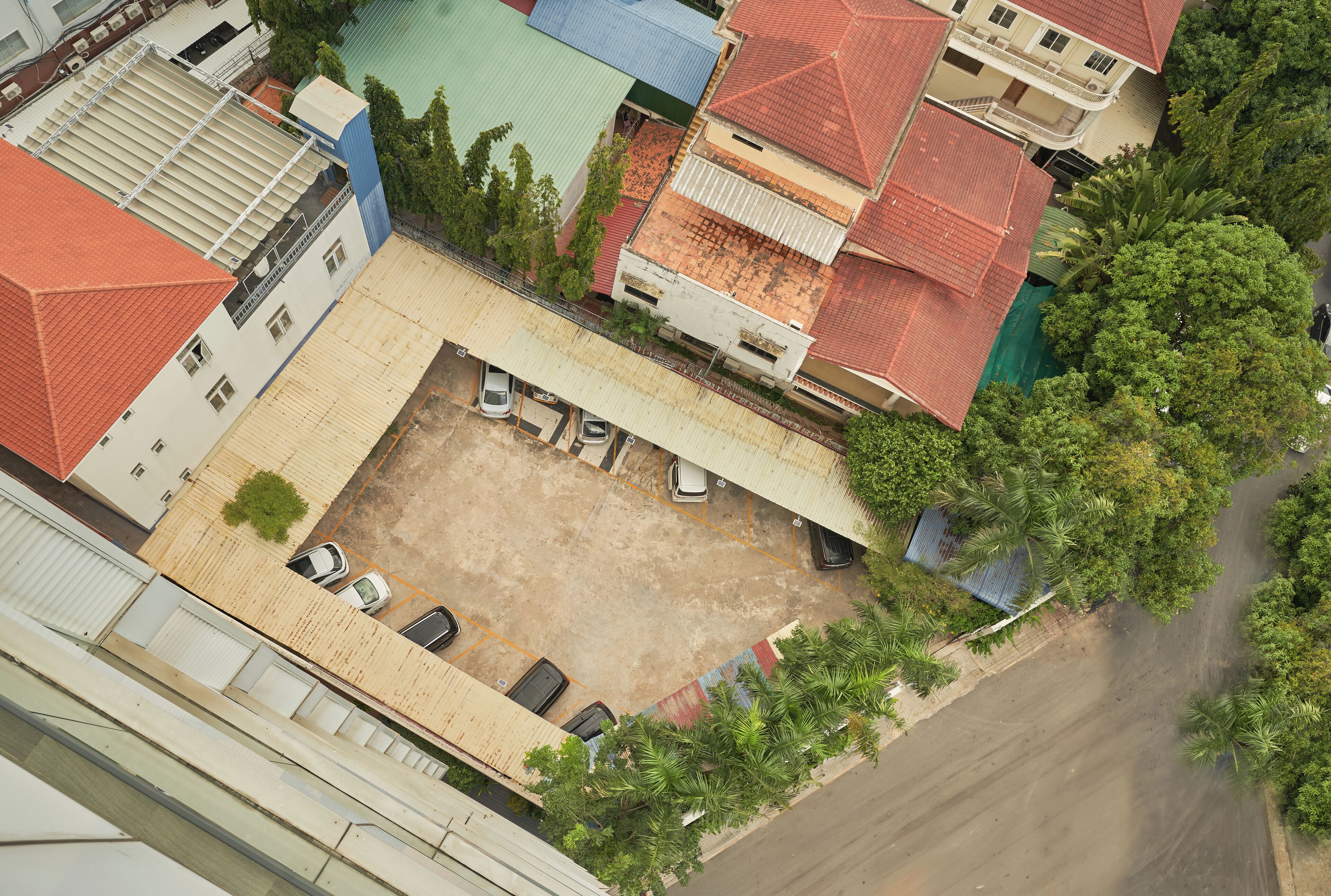 Vista aérea de un patio con zona de estacionamiento, rodeado de edificios con techos rojos y verdes.