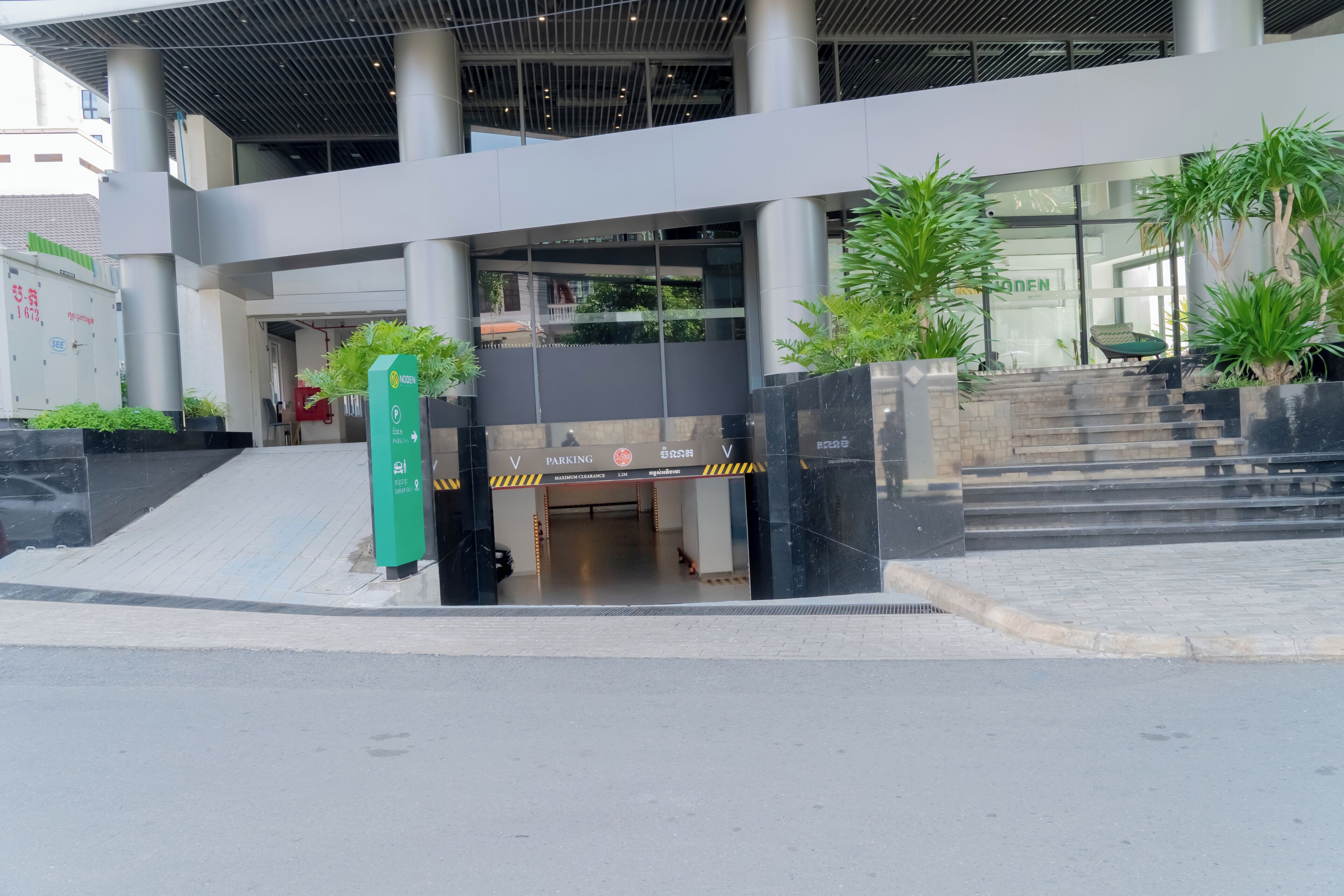 Entrada d'un edifici modern amb façana de vidre, zona d'aparcament i escala que hi condueix.