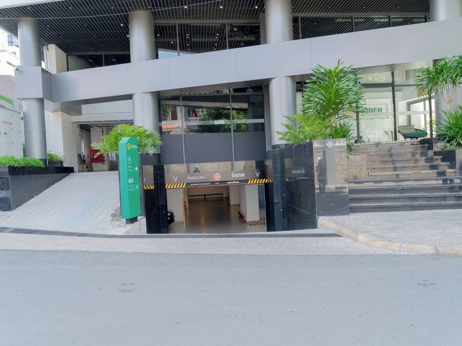 Entrada d'un edifici modern amb façana de vidre, zona d'aparcament i escala que hi condueix.