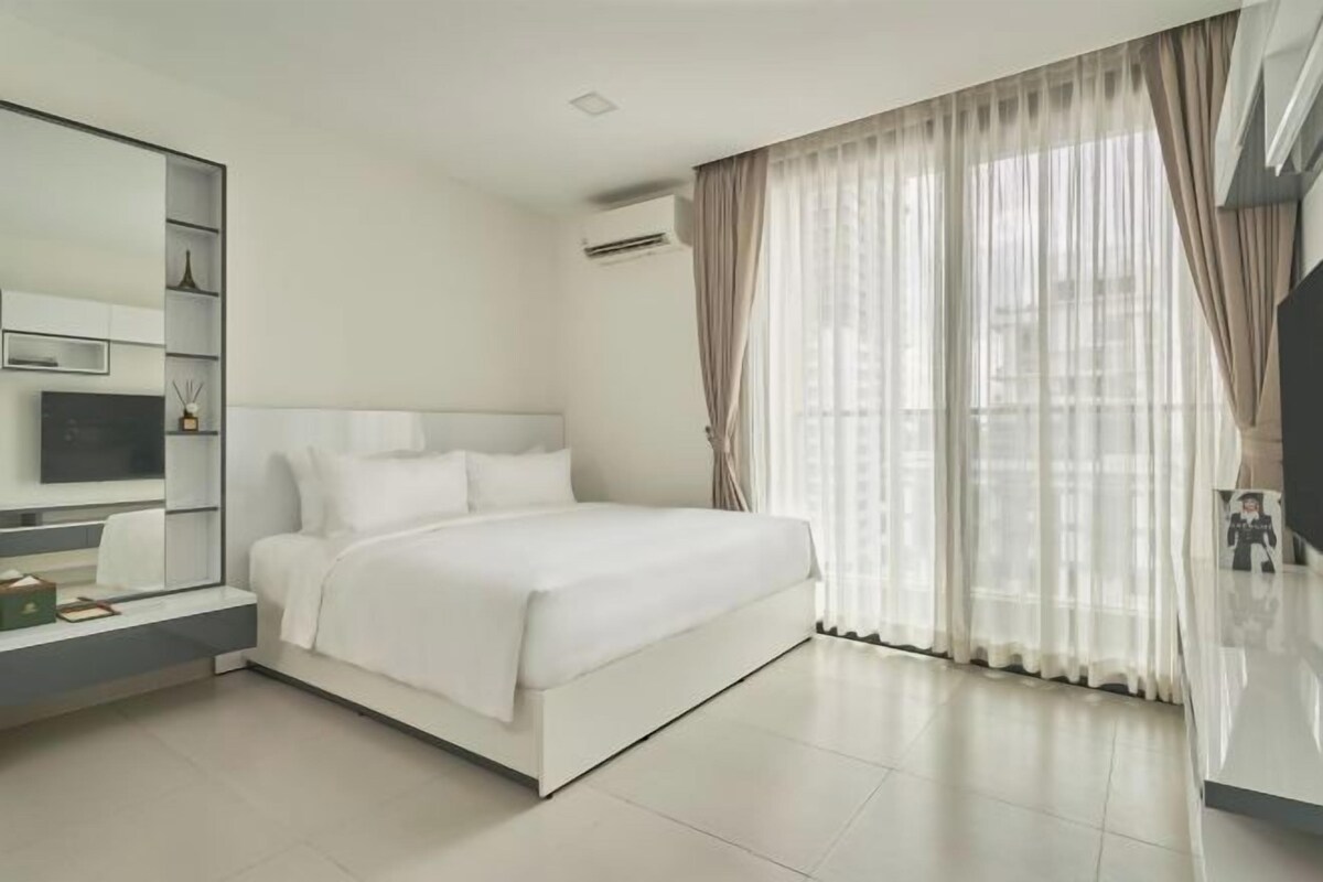 A modern bedroom with a large bed, a TV on a stand, and a built-in shelf unit.