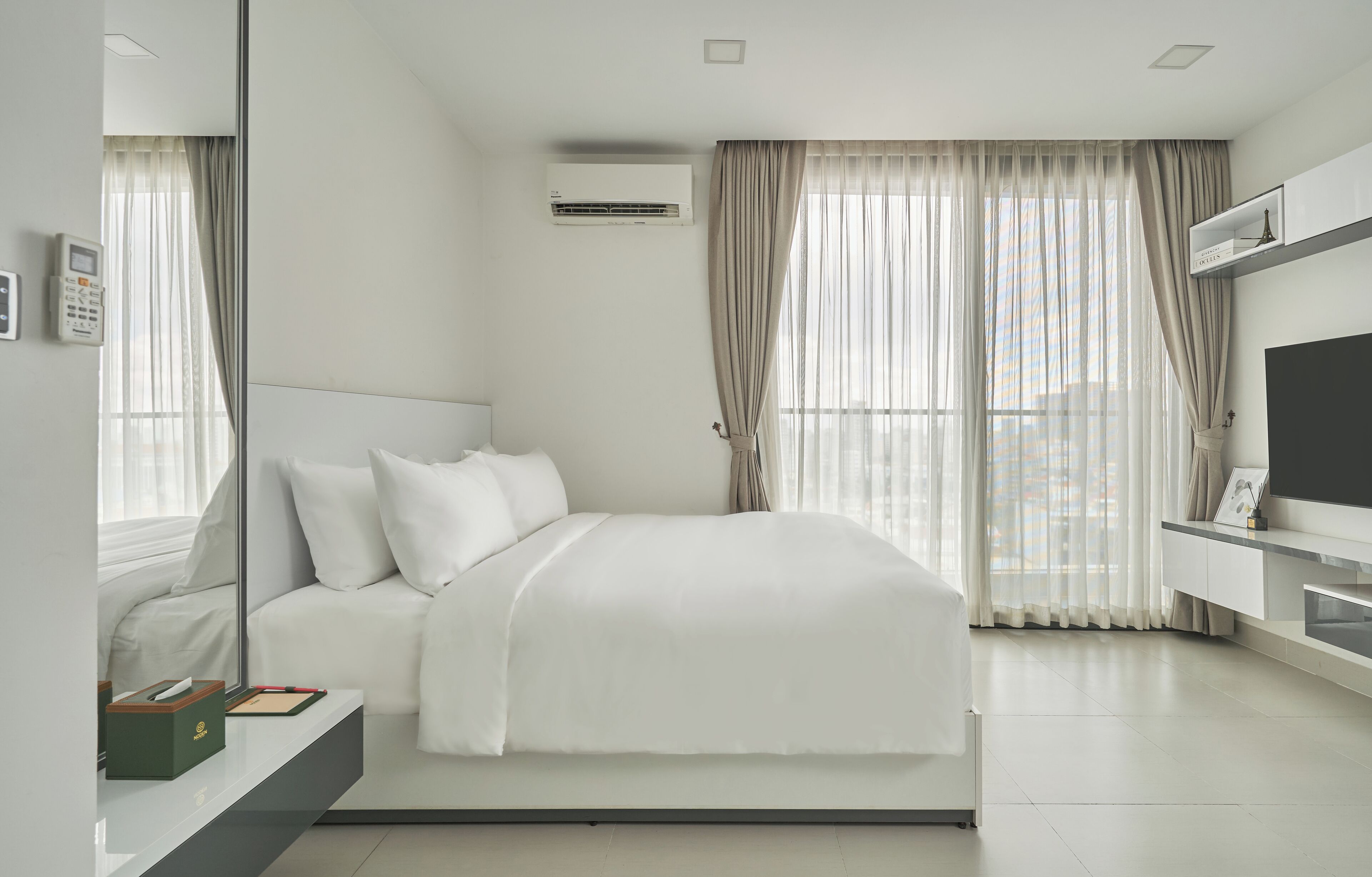 A modern hotel room with a large bed, a TV, a desk, and a window with curtains.
