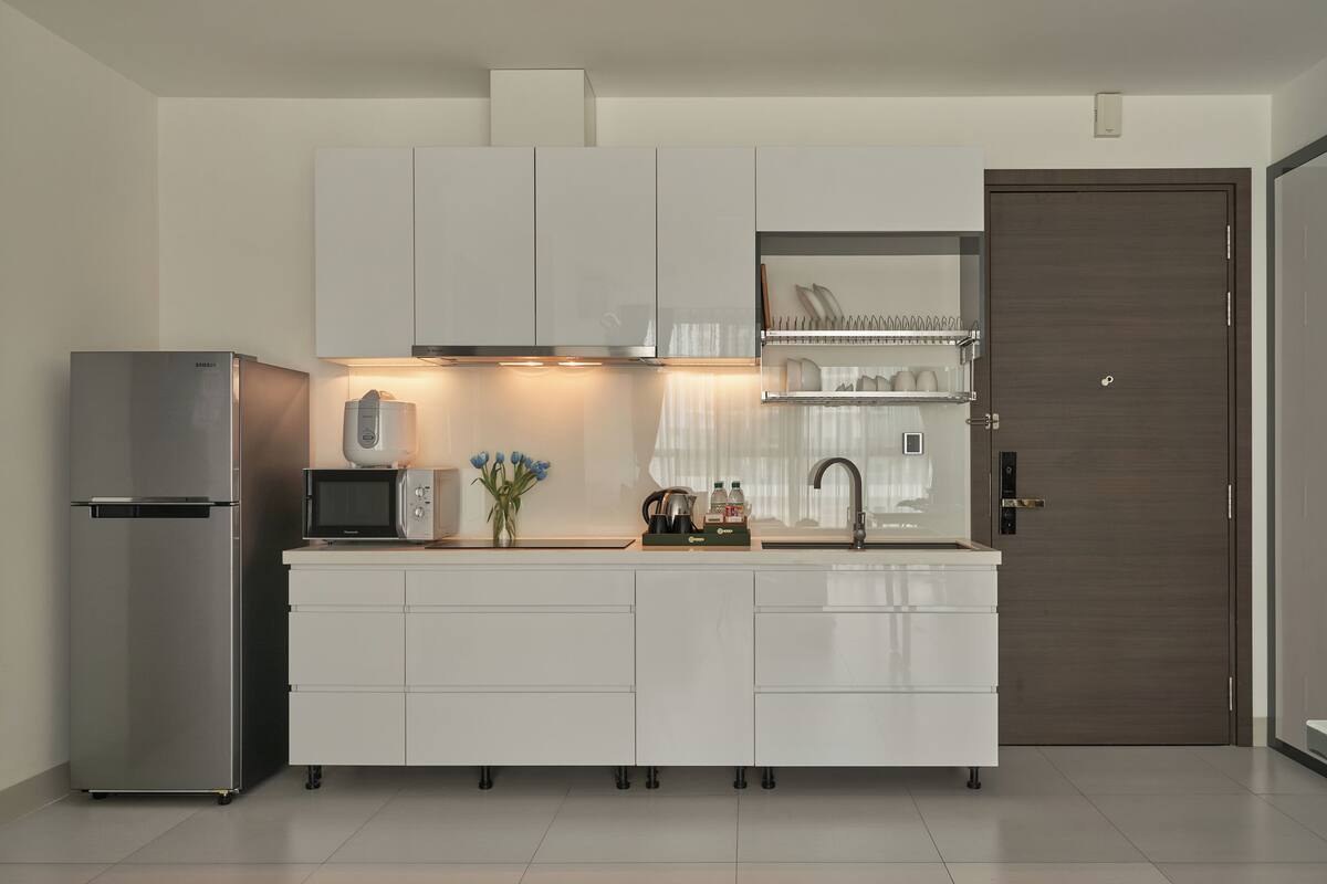 A modern kitchen with white cabinetry, a stainless steel refrigerator, a microwave, and a sink.