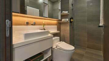 A modern bathroom with a white sink, toilet, and shower. There is a towel rack above the sink and a shelf with toiletries.