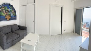 A modern living room with a grey sofa, a white coffee table, and a sliding glass door leading to a balcony. - Panoramic penthouse with sea view (Positano)