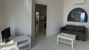 A living room with a TV on a white entertainment unit, a grey sofa, and a white coffee table. - Panoramic penthouse with sea view (Positano)