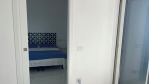 A bedroom with a bed, a patterned headboard, a white wall, a white floor, and a sliding glass door. - Panoramic penthouse with sea view (Positano)
