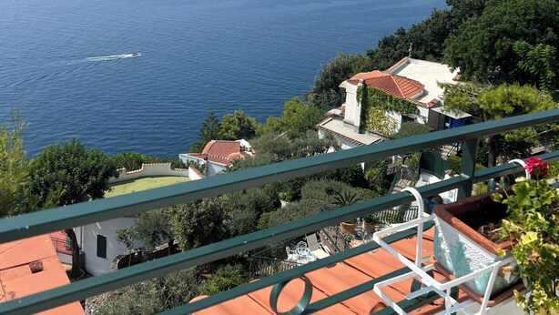 A coastal view with a clear sky, a boat on the water, and buildings with red-tiled roofs. - Panoramic penthouse with sea view (Positano)