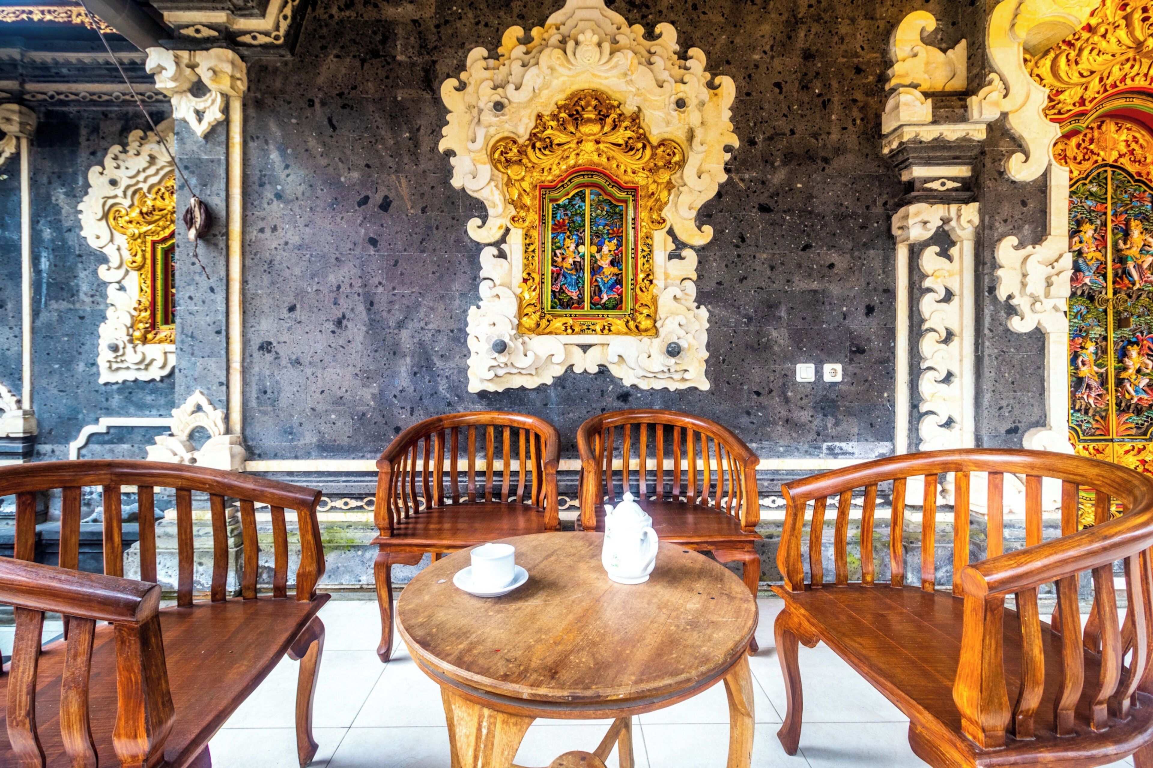 Interior de un templo balinés tradicional con elaboradas esculturas, un altar central y mobiliario de madera.