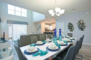 A dining area with a long table set for six, a chandelier, and a view into the kitchen.