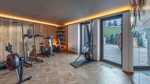 Un gimnasio con diversos equipos de ejercicio, paredes de madera y vistas a un paisaje nevado a través de un ventanal.