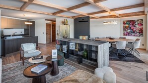 Amplia sala de estar con vigas de madera a la vista, cocina moderna y comedor con una mesa grande y sillas.