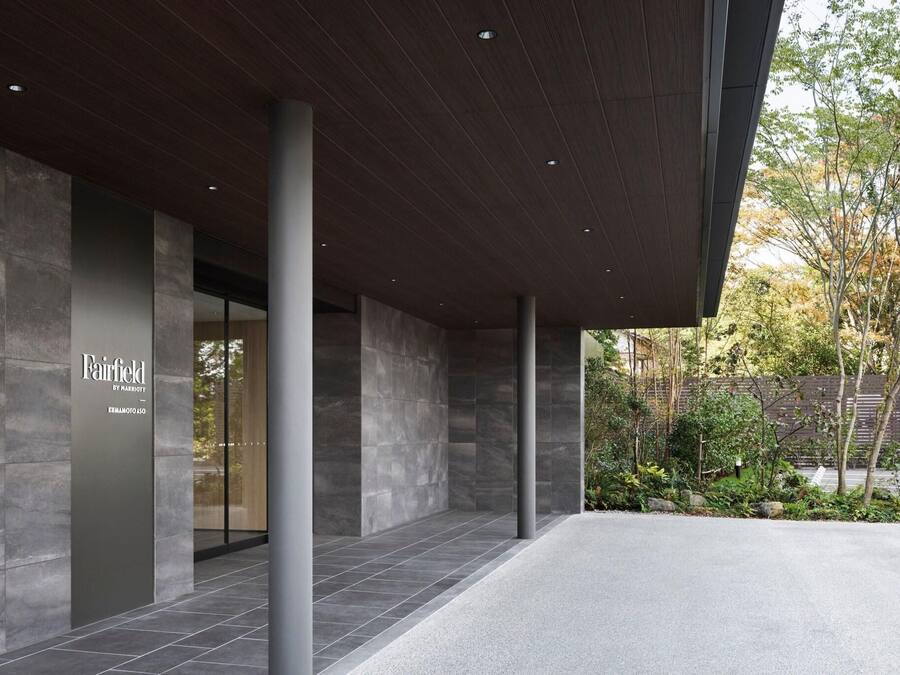 Una entrada moderna a un edificio con fachada de piedra, un letrero de Fairfield by Marriott y un jardín paisajístico.