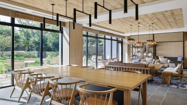 A spacious dining area with a long wooden table and chairs, large windows offering a view of the outdoors, and a modern ceiling design.