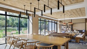 A spacious dining area with a long wooden table and chairs, large windows offering a view of the outdoors, and a modern ceiling design with hanging pendant lights. - Fairfield By Marriott Kumamoto Aso (Aso)