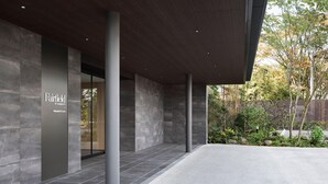 A modern building entrance with a stone facade, a sign for Fairfield by Marriott, and a landscaped garden area. - Fairfield By Marriott Kumamoto Aso (Aso)