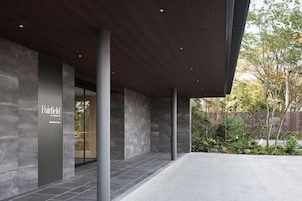 A modern building entrance with a stone facade, a sign for Fairfield by Marriott, and a landscaped garden area.