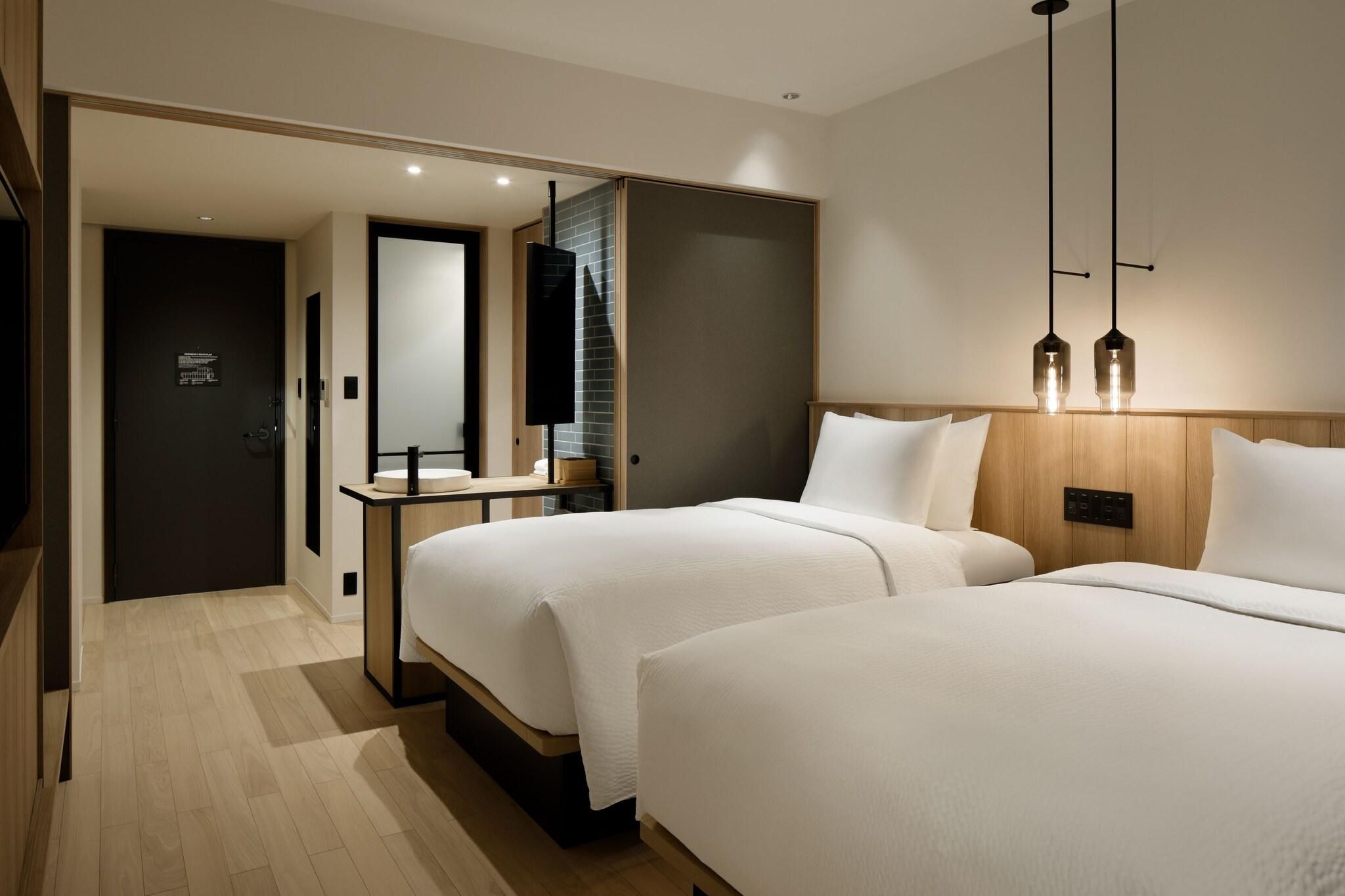 A modern hotel room with two beds, a wooden headboard, a bedside table, and a mirror.