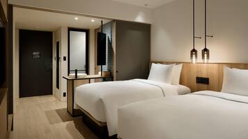 A modern hotel room with two beds, a wooden headboard, a bedside table, and a mirror.