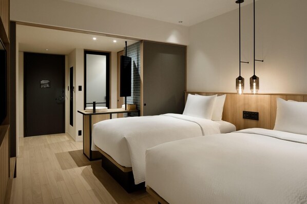 A modern hotel room with two beds, a wooden headboard, a bedside table, and a mirror. - Fairfield By Marriott Kumamoto Aso (Aso)