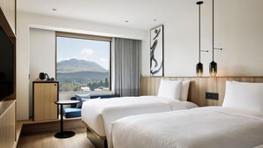 Une chambre d’hôtel avec deux lits, une petite table, un téléviseur et une grande fenêtre donnant sur la montagne.