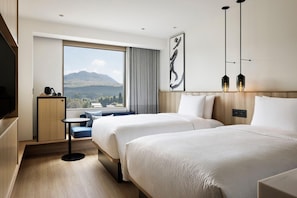A hotel room with two beds, a small table, a TV, and a large window with a mountain view. - Fairfield By Marriott Kumamoto Aso (Aso)
