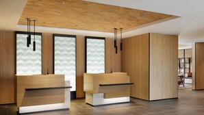 A modern reception area with wooden reception desks, a herringbone-patterned ceiling, and a tiled floor.