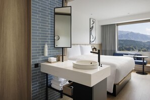 A modern hotel bathroom with a large mirror, white sink, and a view of mountains through the window. - Fairfield By Marriott Kumamoto Aso (Aso)