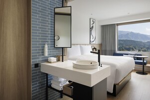 A modern hotel bathroom with a large mirror, white sink, and a view of mountains through the window.