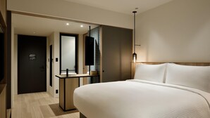 A modern hotel room with a large bed, a bedside table, a mirror, and a small bathroom area with a sink and towel rack. - Fairfield By Marriott Kumamoto Aso (Aso)