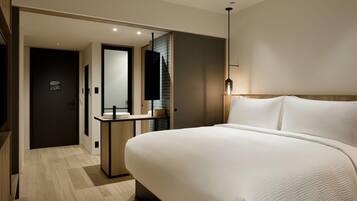 A modern hotel room with a large bed, a bedside table, a mirror, and a small bathroom area with a sink and towel rack.