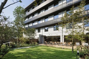 Un edificio de varios pisos con un diseño arquitectónico moderno, que cuenta con una terraza en la azotea y mobiliario exterior.