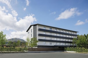 A multi-story hotel with a flat roof and a modern design, featuring a large parking area in front.