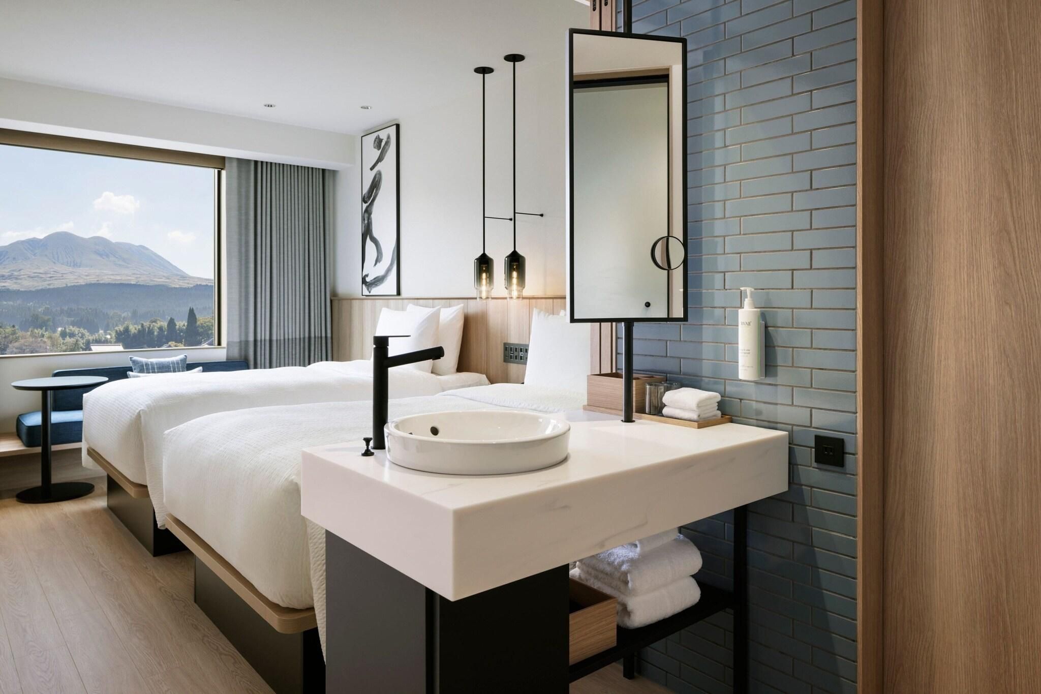 A modern hotel room with a large bed, a round sink, a mirror, and a view of a mountain.