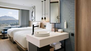 A modern hotel room with a large bed, a round sink, a mirror, and a view of a mountain.