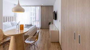 A modern hotel room with a bed, bedside table, and a dining area with a table and chairs.