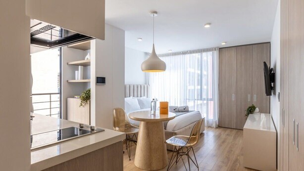 A modern hotel room with a dining area, a sofa, and a TV.