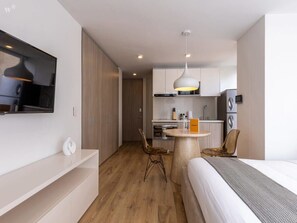 A modern hotel room with a bed, a TV mounted on the wall, a dining area with a table and chairs, and a kitchenette. - w* | Greatest Loft in Santa Ana (Bogotá)