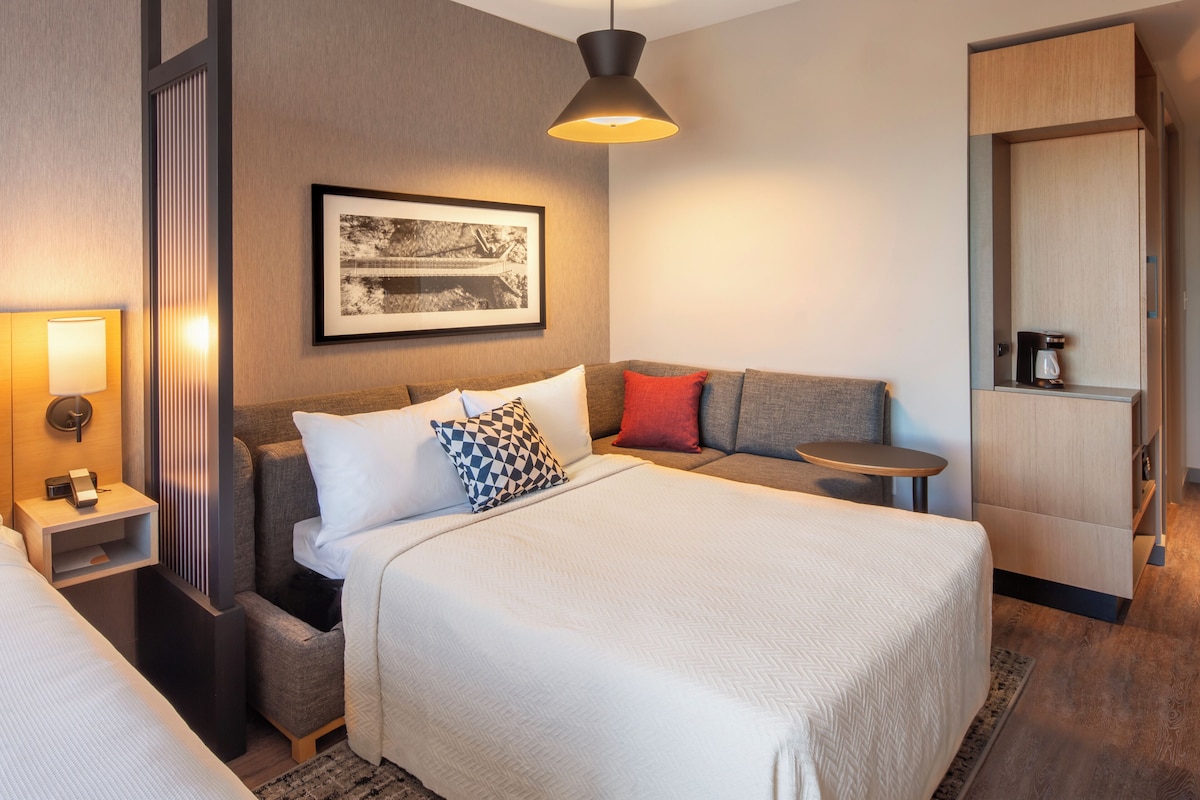 Ein Hotelzimmer mit einem großen Bett, einer Couch, einem kleinen Tisch, einer Lampe, einem gerahmten Bild an der Wand und einem Kleiderschrank.