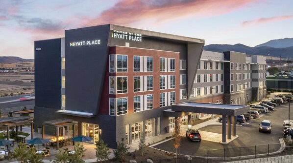 A modern hotel with a prominent 'Hyatt Place' sign, a parking lot, and a view of mountains in the background. - Hyatt Place Reno (Reno)