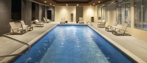 A swimming pool with lounge chairs and a tiled floor.