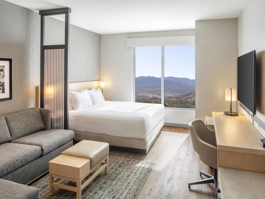 Quarto de hotel moderno com uma cama grande, um sofá, uma escrivaninha e uma televisão.