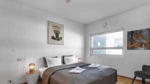 A bedroom with a large bed, bedside lamps, a window, and artwork on the walls.