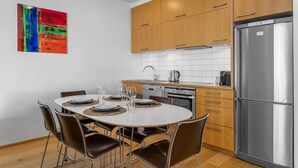 A modern kitchen with wooden cabinets, a stainless steel refrigerator, and a dining table set for four.